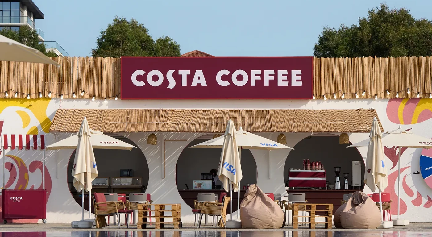 Павильон Costa Coffee на курорте Sea Breeze: три круглые арки, тростниковая крыша, бордовая вывеска и гирлянда лампочек